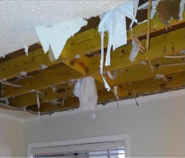 Water damaged drywall on the ceiling in a home has been cut away revealing wet wood structure above.