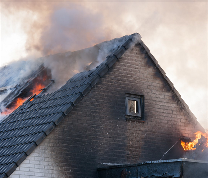 the roof of a house on fire with smoke and flames billowing from its windows
