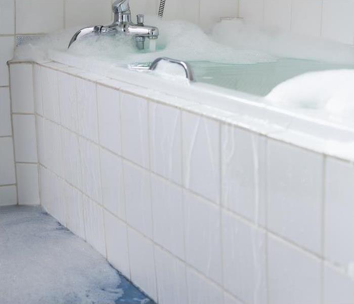 White tile bathtub overflowing water and bubbles onto a blue tile floor